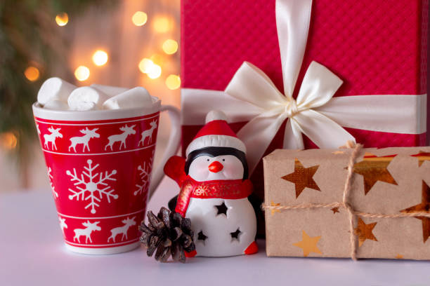 un pingüino de regalo con un sombrero de papá noel cerca de una caja de regalo de navidad, una taza con malvaviscos. decoraciones de año nuevo - coffee bean coffee flower ribbon fotografías e imágenes de stock