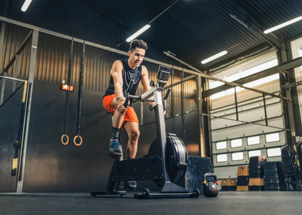 Male athlete exercising on bike in gym Handsome male athlete on exercise bike in gym. Sportsman is doing endurance training. He is in illuminated health club. cardiovascular exercise stock pictures, royalty-free photos & images