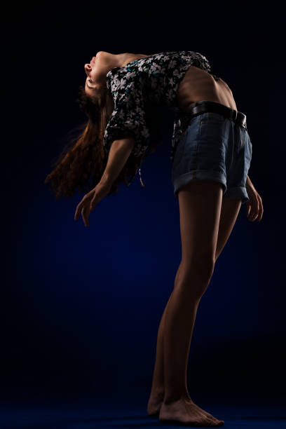 Young flexible girl posing against dark blue background. Ballet dancing pose.