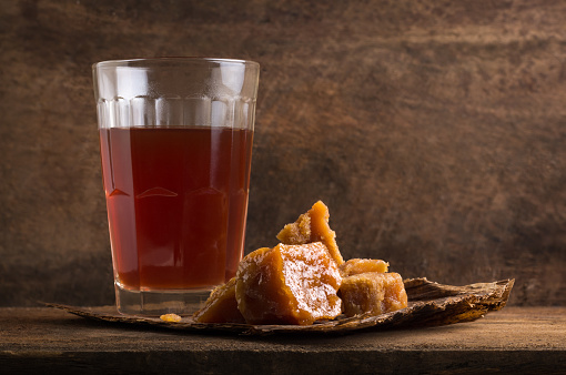 pieces of jaggery or unrefined sugar or palm sugar with a glass of tea, traditional sweetener in southeast asia with a hot drink on wooden surface, moody concept
