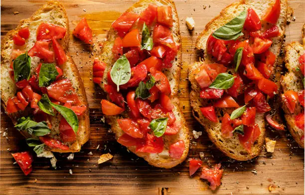Italian bruschetta on a rustic wood cutting board. Grilled sliced rustic bread topped with extra virgin olive oil, tomato, and origan