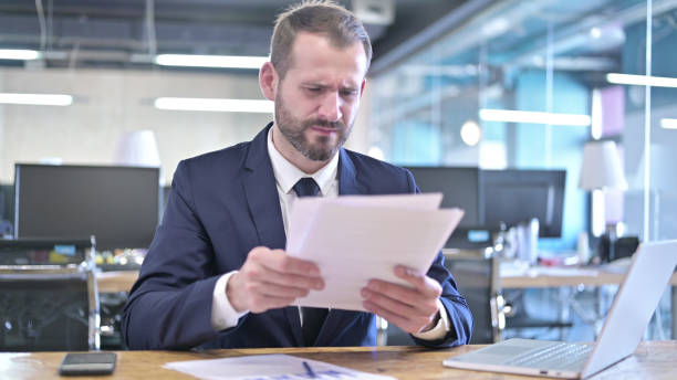 istock Upset Young Businessman Reading the Documents in Office 1344946826