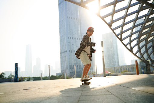 teenage asian child skateboarding outdoors on city square with modern building in background