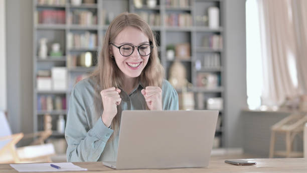 istock Surprised Woman Celebrating with both Fist while sitting in Office 1344948331