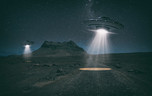 Two old-style UFO hover over a desert landscape at night, probing the ground with bright lights. Miniature photography.