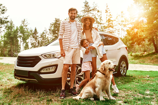 The whole family came to nature for the weekend. Mom and Dad with their daughter and a Labrador dog are standing near the car. Leisure, travel, tourism.