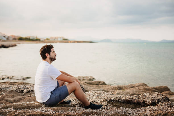 istock Handsome young man sitting thoughtful on the beach looking in the far 1344954774