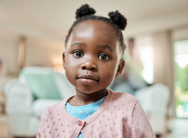 beschnittenes porträt eines entzückenden kleinen mädchens mit zöpfen, das zu hause auf dem wohnzimmerboden sitzt - little girls african descent black small stock-fotos und bilder