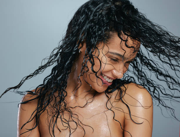 scatto in studio di una giovane donna attraente che si snoda i capelli bagnati su uno sfondo grigio - riccio foto e immagini stock