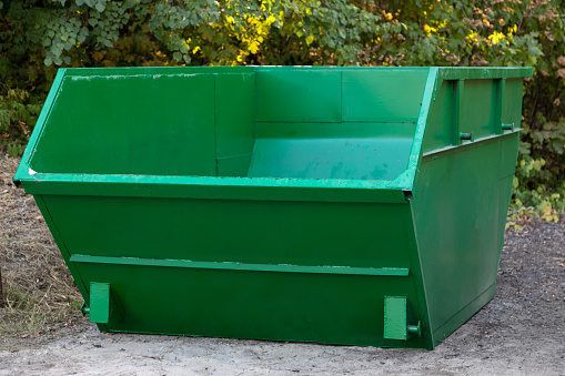 empty large green metal container for construction or other large-sized garbage against background of trees in park. Concept of environmental protection