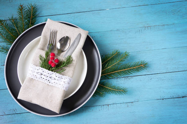 istock Christmas table setting- plates, table fork and knife set with napkin, fir branches and red berries white on blue wooden board 1344963728