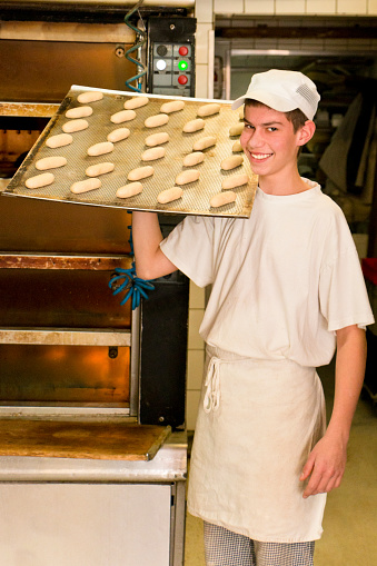 Baker trainee posing with a baking sheet full of buns in front a the oven.