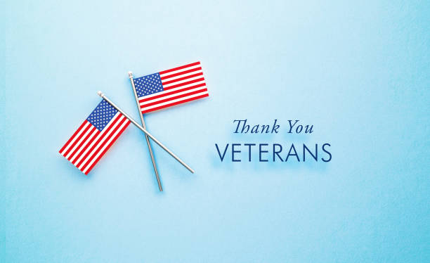 Thank You Veteran's message sitting next to tiny American flag pair on blue background. Horizontal composition with copy space. Directly above. US Veteran's Day concept.