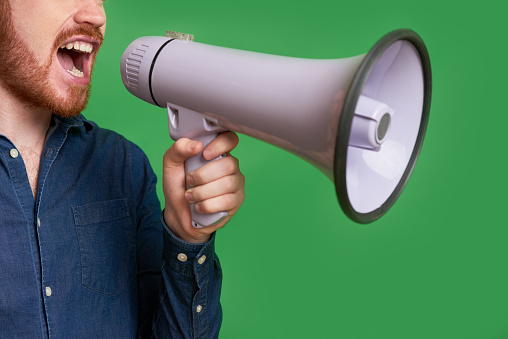 Close-up of bearded man screaming through loudspeaker against green background
