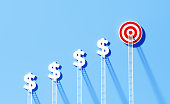 istock White Ladders Leaning Onto Dollar Signs And Bull's Eye Target on Blue Wall 1344967987