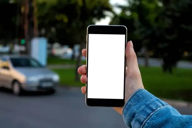Photo of Mockup image of woman hand holding mobile phone with blank white desktop screen. Blurry city view in the background.