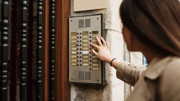Young woman calling an apartment intercom at the entrance of a residential building in a city