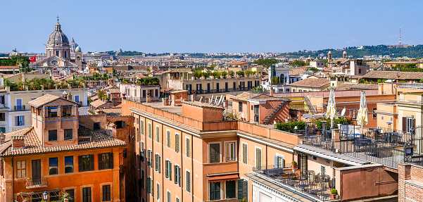 A suggestive and detailed view over the rooftops of Rome in a wide-angle image taken from the terrace of the monumental staircase of Trinità dei Monti, better known as Spanish Steps, in the historic and baroque heart of the Eternal City. On the horizon the dome of the Basilica of Santi Ambrogio e Carlo, along Via del Corso. In 1980 the historic center of Rome was declared a World Heritage Site by Unesco. Image in High Definition format.
