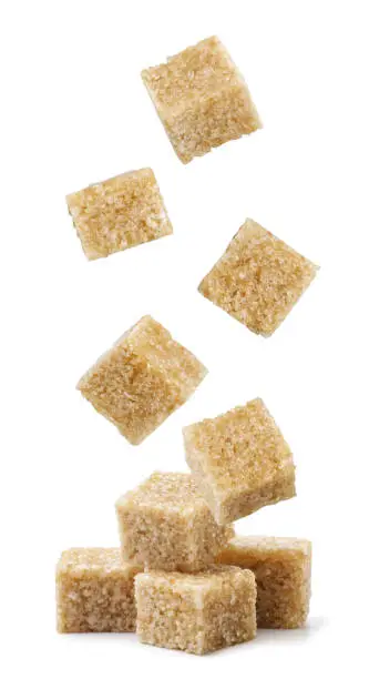 Cane sugar cubes fall on a heap close-up on a white background. Isolated