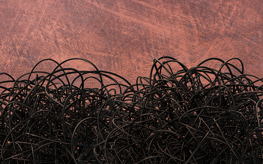 Large amount of tangled black cable on a rusty wall background. Excess and confusion.