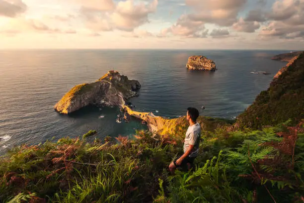 Photo of Young caucasian woman looking to Gaztelugatxe ermitage at Basque Country coast.