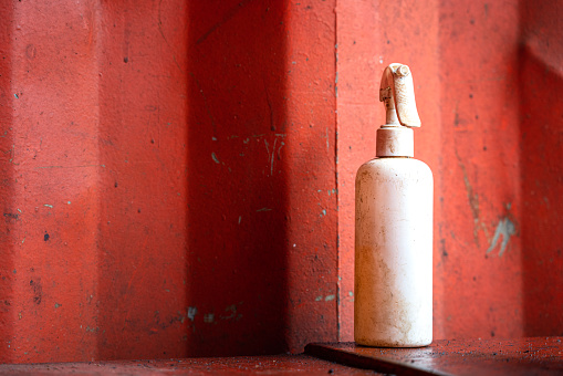 A white cleaner chemical spray bottle for using in mechnical repairing work, It is placed on workbench near metal orange wall container. Industrial equipment object photo. Selective focus.