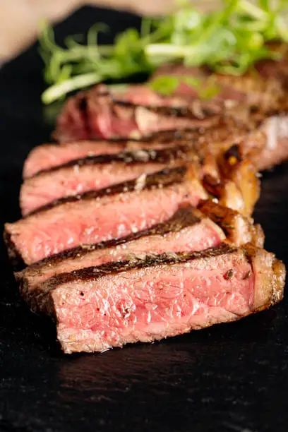 Sliced medium-rare steak served on a piece of slate. Colour, vertical with some copy space.