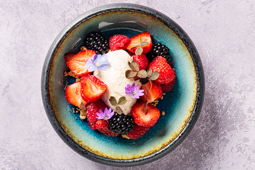 Summer fruits; strawberries, blackberries and raspberries, served with organic vanilla ice cream and decorated with wood sorrel and a sprinkling of crushed nuts. Colour, horizontal format with some copy space.