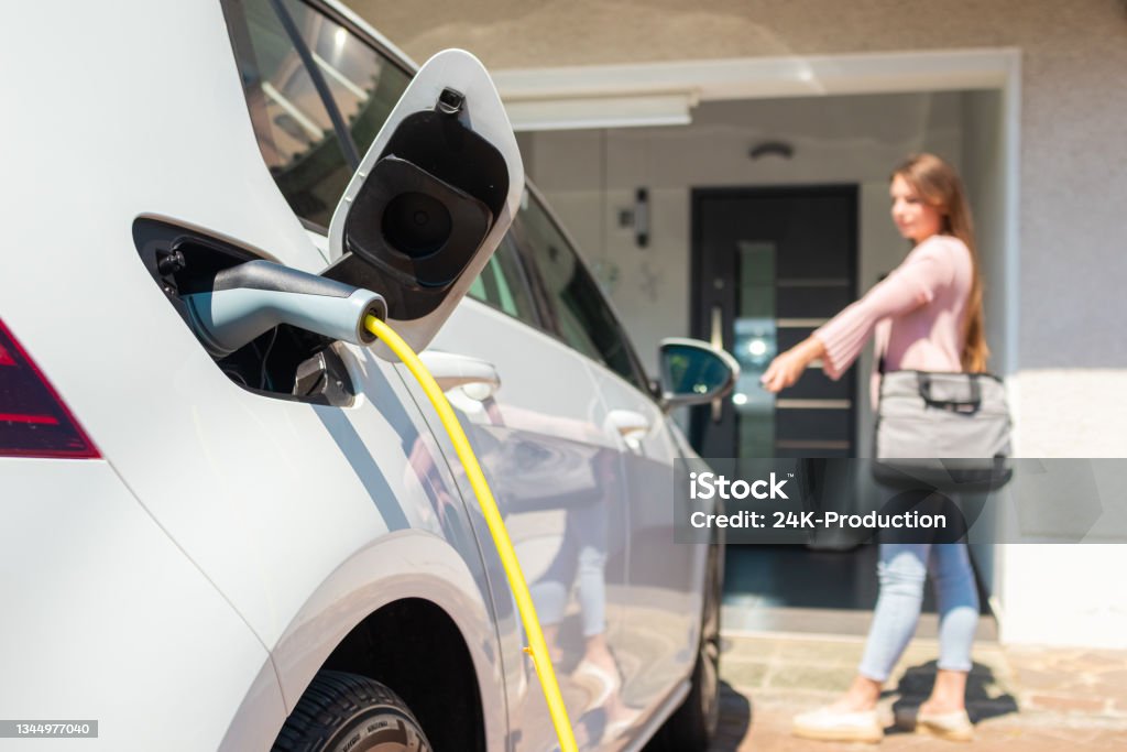 EV Charger station at home Woman charging electric car at home with cable. Electric Car Stock Photo