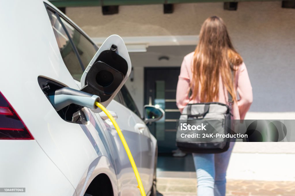Electric car charger plugged in Electric car charger plugged in, with a female silhouette in the background Electric Vehicle Stock Photo