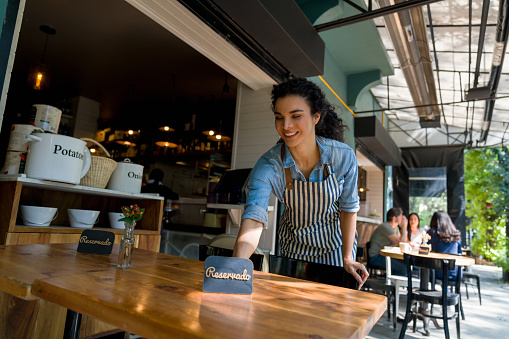 Happy waitress putting a reserved sign on a table while working at a restaurant - food service concepts