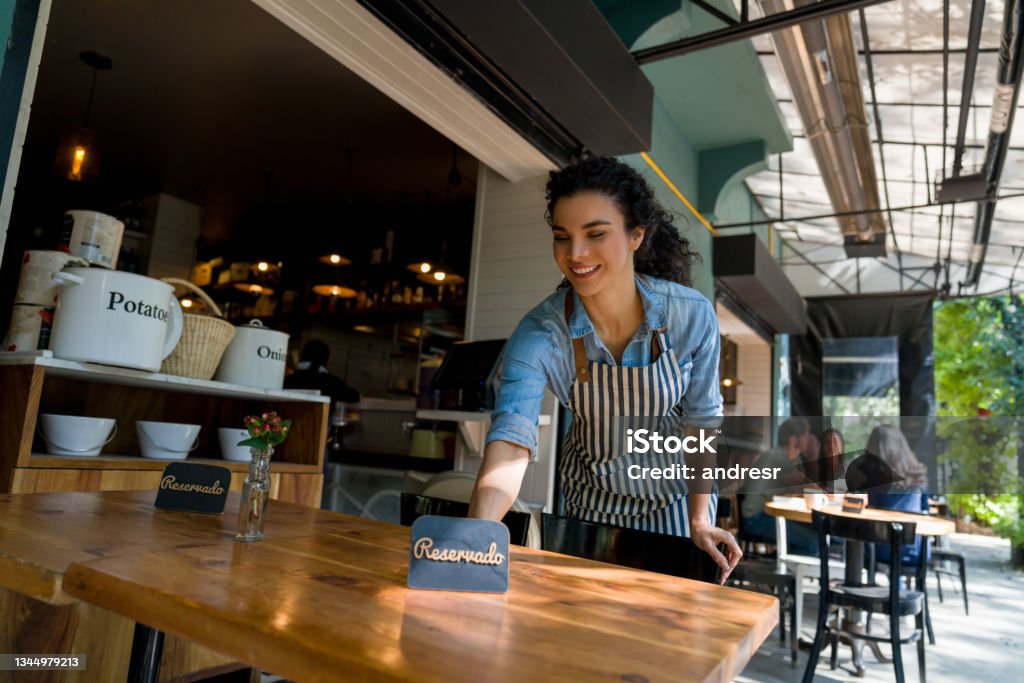 Waitress putting a reserved sign on a table at a restaurant Happy waitress putting a reserved sign on a table while working at a restaurant - food service concepts Reserved Sign Stock Photo