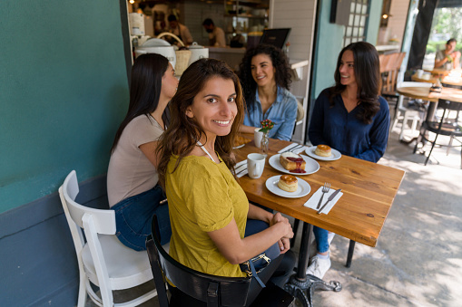 Happy woman meeting a group of friends at a cafe and eating desserts while looking at the camera smiling - lifestyle concepts