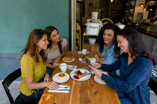 Happy group of women meeting at a coffee shop and laughing after watching something on social media
