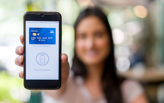 Happy Latin American woman holding her cell phone to make an NFC payment - technology in small business concepts. **DESIGN ON SCREEN BELONGS TO US**