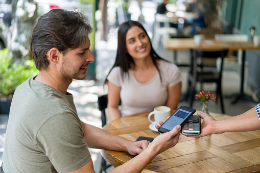 Happy Latin American man at a restaurant making a contactless payment with his cell phone - technology concepts. **DESIGN ON SCREEN BELONGS TO US**