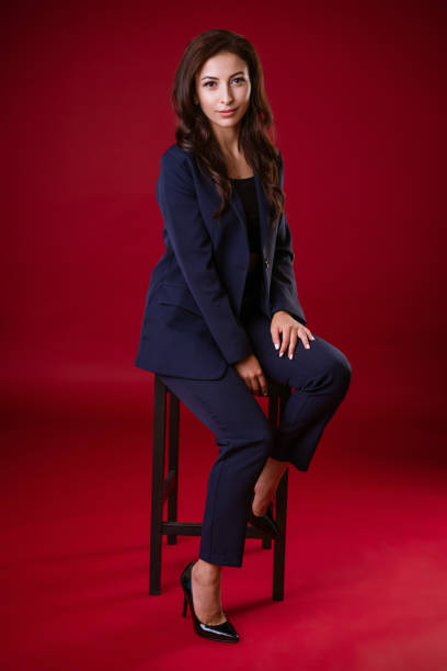 business woman in suit posing on chair on red background - fato de senhora imagens e fotografias de stock