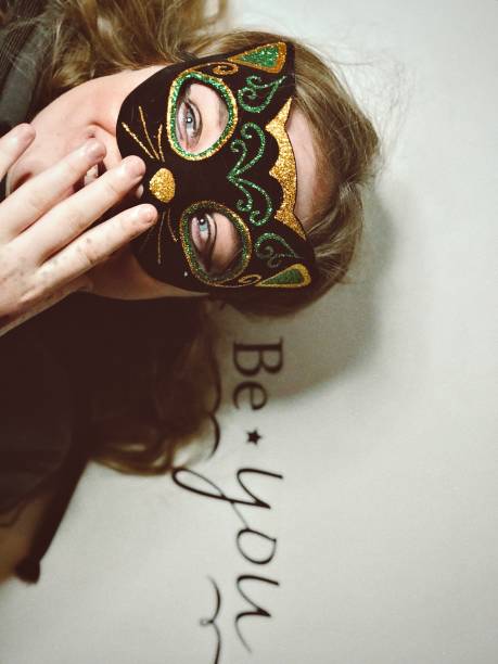 Cute teen girl with cat mask on, smiling and laying on a “Be You” sign. stock photo