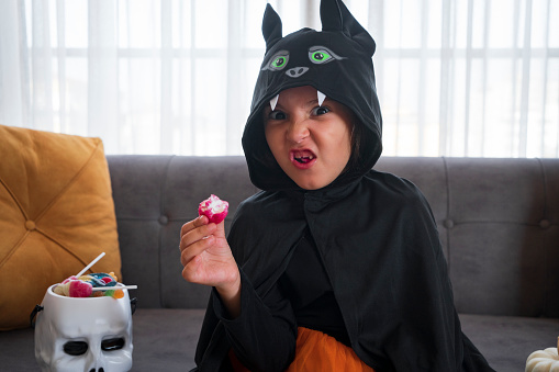 Cute girl wearing Halloween costumes, playing and eating candies at home.