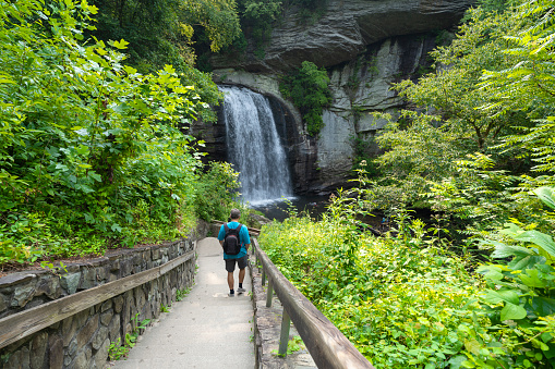 Hiker with backpack walking on the path  to the waterfall. Looking Glass Falls near Brevard, Pisgah National Forest, North Carolina, USA.
