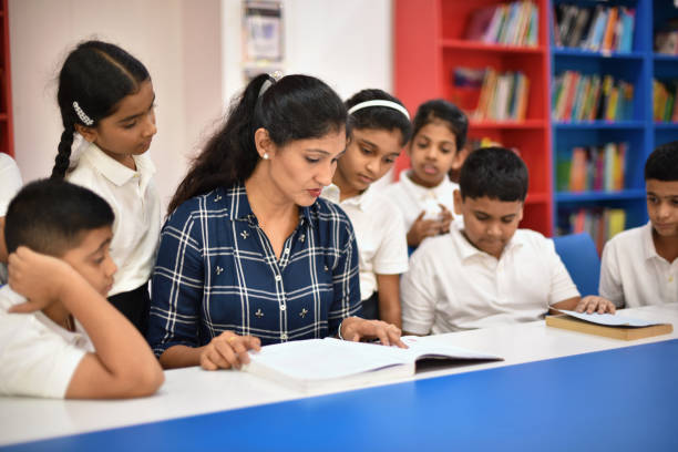 istock Teacher reading book to students sitting in a school library 1344985960