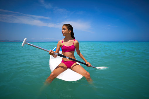 Girl relaxed sitting on paddle surf board SUP in summer
