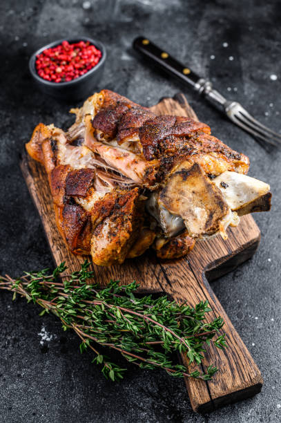 istock Roasted pork knuckle eisbein on a wooden board with herbs. Black background. Top view 1344992641