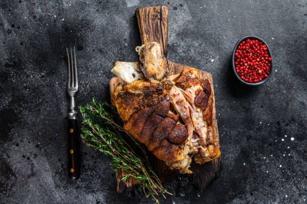 istock Roasted pork knuckle eisbein on a wooden board with herbs. Black background. Top view 1344992659