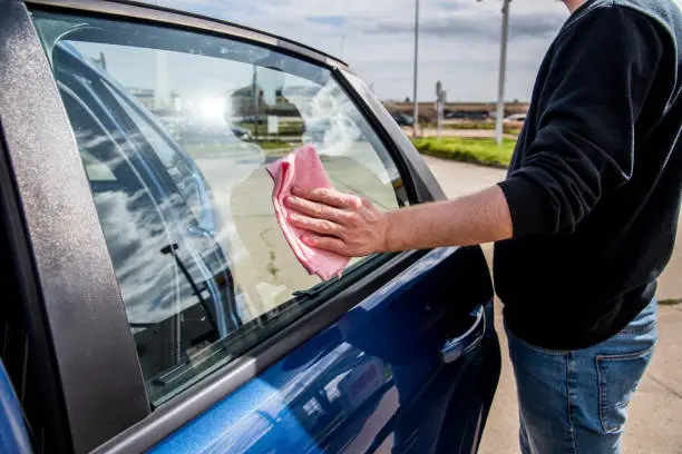 Close-up of a car wash employee cleaning the exterior of the window of a car using a pink wipe cloth