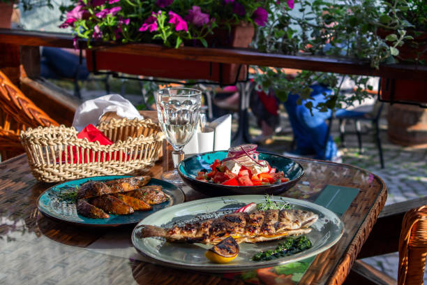 istock server table with a freshly prepared three-course lunch on the summer terrace of the cafe. Grilled trout, grilled potatoes, fresh tomato, pepper and onion salad, a glass of white wine. Tasting. 1344994132