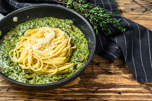 Spaghetti pasta with spinach in cream sauce with parmesan in a pan. Wooden background. Top view. Copy space.