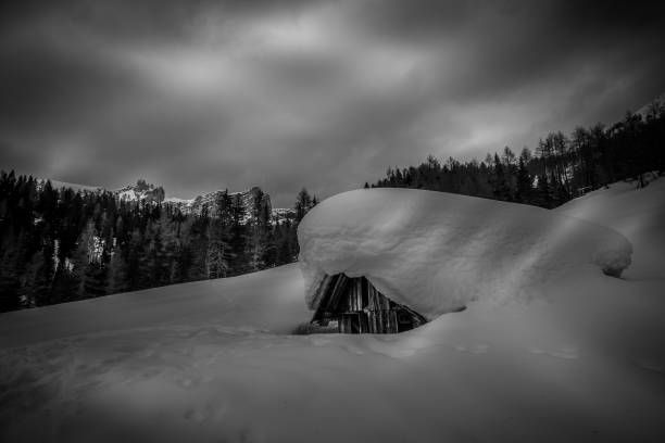istock Black and white effect of small mountain hut almost completely buried by snow 1344996411