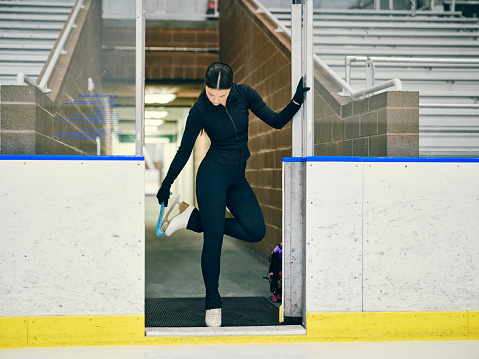 A young woman competitive figure skater training in an empty ice rink arena.