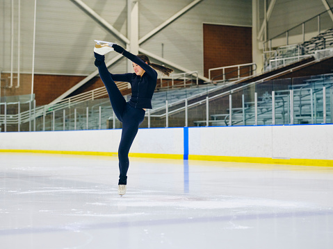 A young woman competitive figure skater training in an empty ice rink arena.